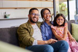Família sorridente reunida no sofá, representando união e planejamento familiar para o futuro dos filhos.