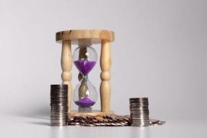 Pilhas de moedas ao lado de ampulheta simbolizando liquidez financeira ao vender uma cota de consórcio.