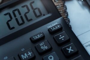 Calculadora exibindo o ano 2026 ao lado de documentos financeiros e moedas, simbolizando planejamento e investimentos.