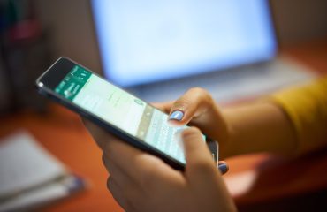 Pessoa usando WhatsApp no celular enquanto digita mensagem, representando cuidados com segurança digital e golpes no aplicativo.