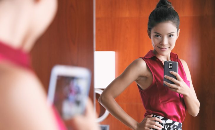 Mulher tirando selfie no espelho, simbolizando a dismorfia financeira e a percepção distorcida da própria situação econômica.