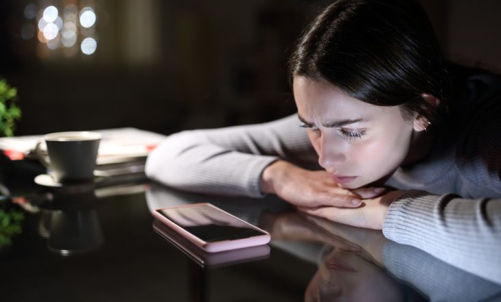Mulher triste olhando o celular, representando o ghosting econômico e o impacto do endividamento nas relações pessoais.